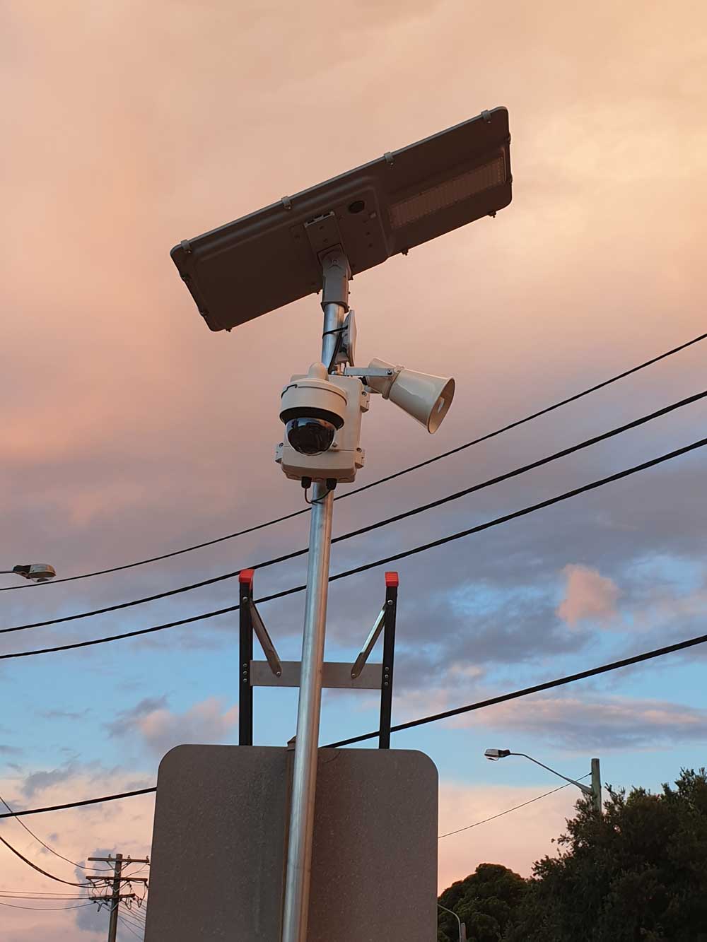 A pole camera with solar panel and light at dusk against an orange sky