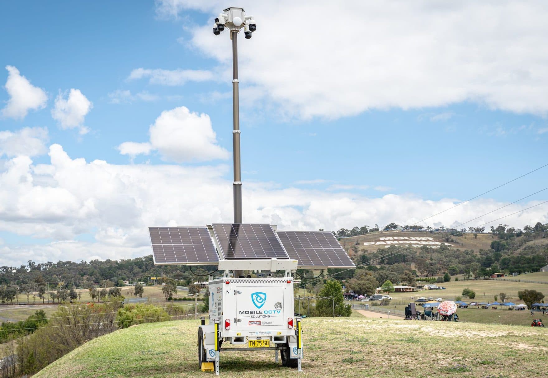 A Mobile CCTV Solutions trailer with raised camera mast and solar panels deployed on a grassy hill